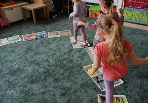 Dziewczynki chodzą po gazetach rozłożonych na dywanie