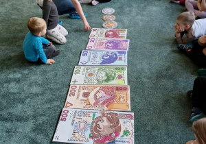 Dzieci siedzą wokół symbolicznych monet i banknotów będących w obiegu w Polsce