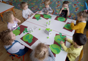 Sala. Przedszkolna dzieci siedzą przy stolikach i wykonują pracę plastyczną ,,Mój dinozaur".