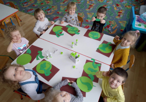 Sala. Przedszkolna dzieci siedzą przy stolikach i wykonują pracę plastyczną ,,Mój dinozaur".