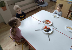 Sala przedszkolna. Dzieci siedzą przy stole próbują hiszpańskie produkty.