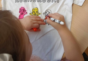 Dziewczynka koloruje obrazki na koszulce z napisem "Różnorodni"