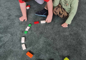 Chłopcy układają na dywanie kształt koła z klocków LEGO