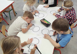 Dzieci podczas wykonywania pracy plastycznej przy stolikach.
