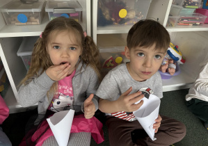 dzieci w sali przedszkolnej jedzą popcorn z papierowych rożków