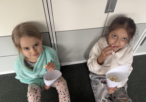 dzieci w sali przedszkolnej jedzą popcorn z papierowych rożków