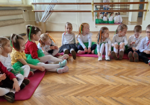 dzieci siedzą na materacach na sali gimnastycznej