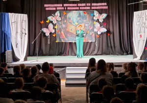 Pani stojąc na scenie opowiada mówi do widzów przez mikrofon