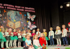 Dzieci stojąc na scenie graja na instrumentach muzycznych