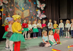 Dzieci stojąc na scenie graja na instrumentach muzycznych