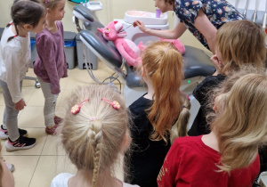 dzieci w gabinecie dentystycznym przyglądają się jak Pani Dentystka sprawdza zęby maskotce