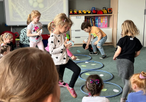 Dzieci podczas zabawy ruchowej w podrzucanie jaj do gniazd (kół hula hop)