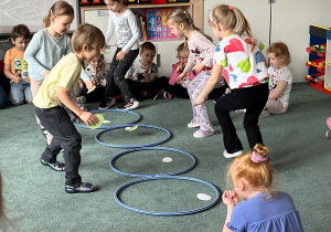 Dzieci podczas zabawy ruchowej w podrzucanie jaj do gniazd (kół hula hop)