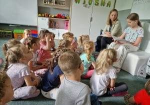 Dzieci słuchają książki czytanej przez siostrę jednej z dziewczynek