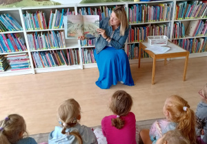 Dzieci słuchają książki czytanej przez panią bibliotekarkę