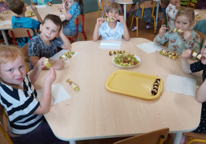 Dzieci zajadają się samodzielnie przygotowanymi szaszłykami owocowymi