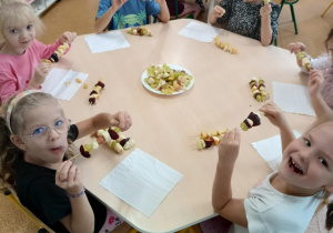 Dzieci zajadają się samodzielnie przygotowanymi szaszłykami owocowymi