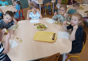 Dzieci zajadają się samodzielnie przygotowanymi szaszłykami owocowymi