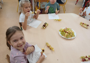 Dzieci zajadają się samodzielnie przygotowanymi szaszłykami owocowymi