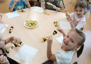 Dzieci zajadają się samodzielnie przygotowanymi szaszłykami owocowymi