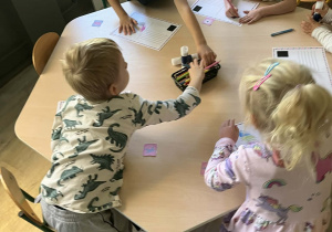Dzieci przy stoliku ozdabiają i adresują swoje pocztówki