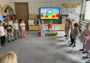 Dzieci w kole podczas urodzin dwójki dzieci siedzących na krzesełkach z prezentami