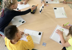 Dzieci kolorujący i ozdabiający przy stoliku pocztówki