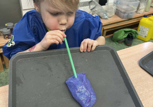 Dziewczynka dmuchająca rurką w masę slime