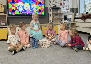 Dzieci siedzące na dywanie z dziewczynką obchodzącą urodziny