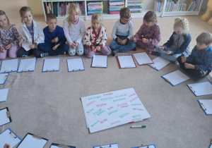 Dzieci siedzą w kole wokół wspólnie stworzonej listy przedszkolnych potworów