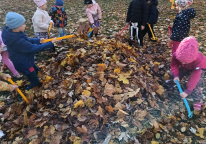Dzieci grabią liście w ogrodzie przedszkolnym