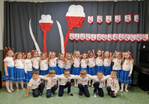 Dzieci z Grupy Sówki pozują do zdjęcia na tle dekoracji przygotowanej z okazji Narodowego Święta Niepodległości