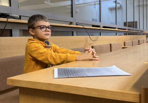 Chłopiec w roli oskarżonego siedzi w ławie sądowej