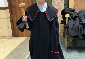 Dziewczynka w todze prokuratora z młotkiem sędziowskim w ręce