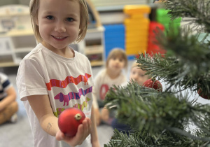 Dziewczynka zawieszająca bombkę na choince w sali