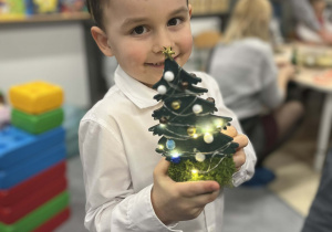 Chłopiec trzymający własnoręcznie wykonaną choinkę pozujący do zdjęcia