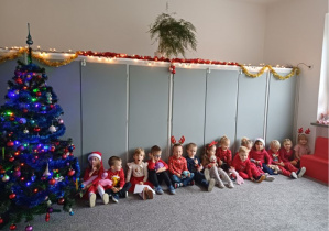 Dzieci siedzą na dywanie przy choince