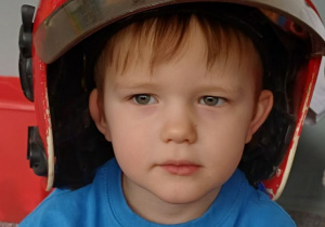 chłopiec pozuje w kasku strażaka