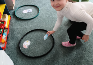 Dziewczynka odkłada obrazek przedstawiający odpad komunalny do czarnego koła