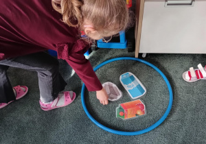 Dziewczynka odkłada obrazek przedstawiający kartonowe pudło do niebieskiego koła