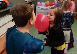 Dziewczynka i chłopiec tańczą z balonem trzymając go między brodami
