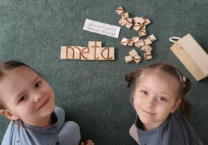 Dziewczynki pozują do zdjęcia z ułożonym z klocków wyrazem "meta"