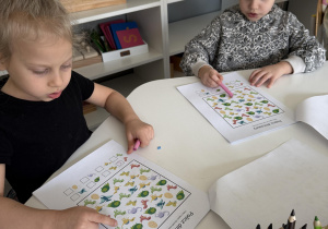 dzieci przy stołach wykonują karty pracy