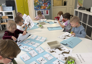 dzieci przy stołach wykonują karty pracy