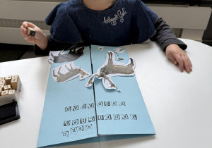 dzieci przy stołach wykonują karty pracy