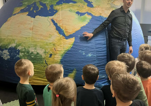 Dzieci przed balonem imitującym kule ziemską na sali gimnastycznej