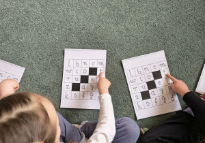 Dziewczynki wskazują na planszy litery odpowiadające głoskom, z których składa się podane przez nauczycielkę słowo