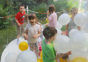 Dzieci w ogrodzie przedszkolnym znajduące się w kuli z balonami