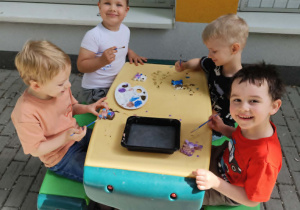 Dzieci przy plastikowym stoliku na tarasie podczas malowania figurek