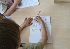 Chłopiec koloruje literę na planszy do gry "Literowe BINGO"
